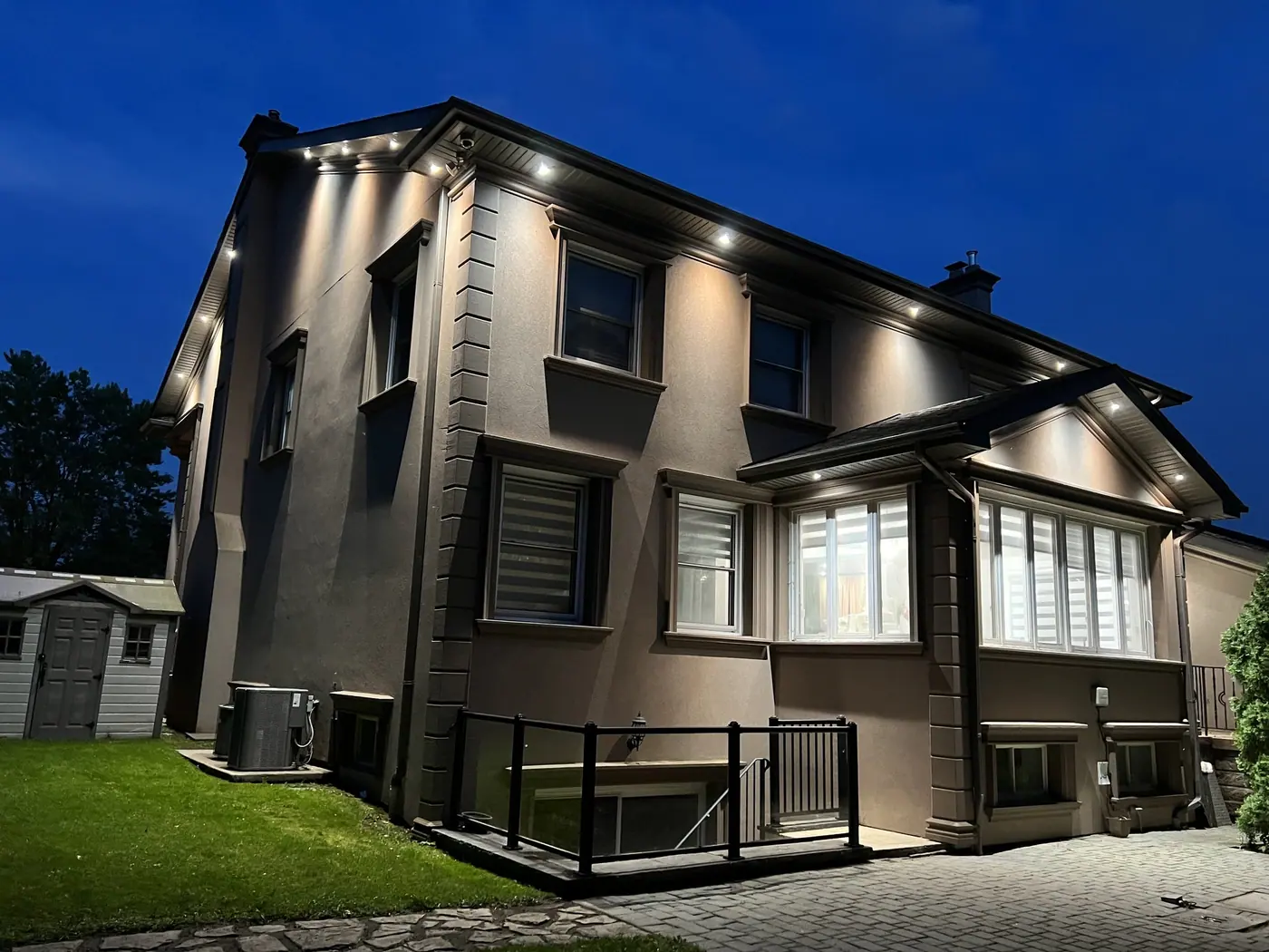 Back of a two-storey home lit by soffit potlights at dusk
